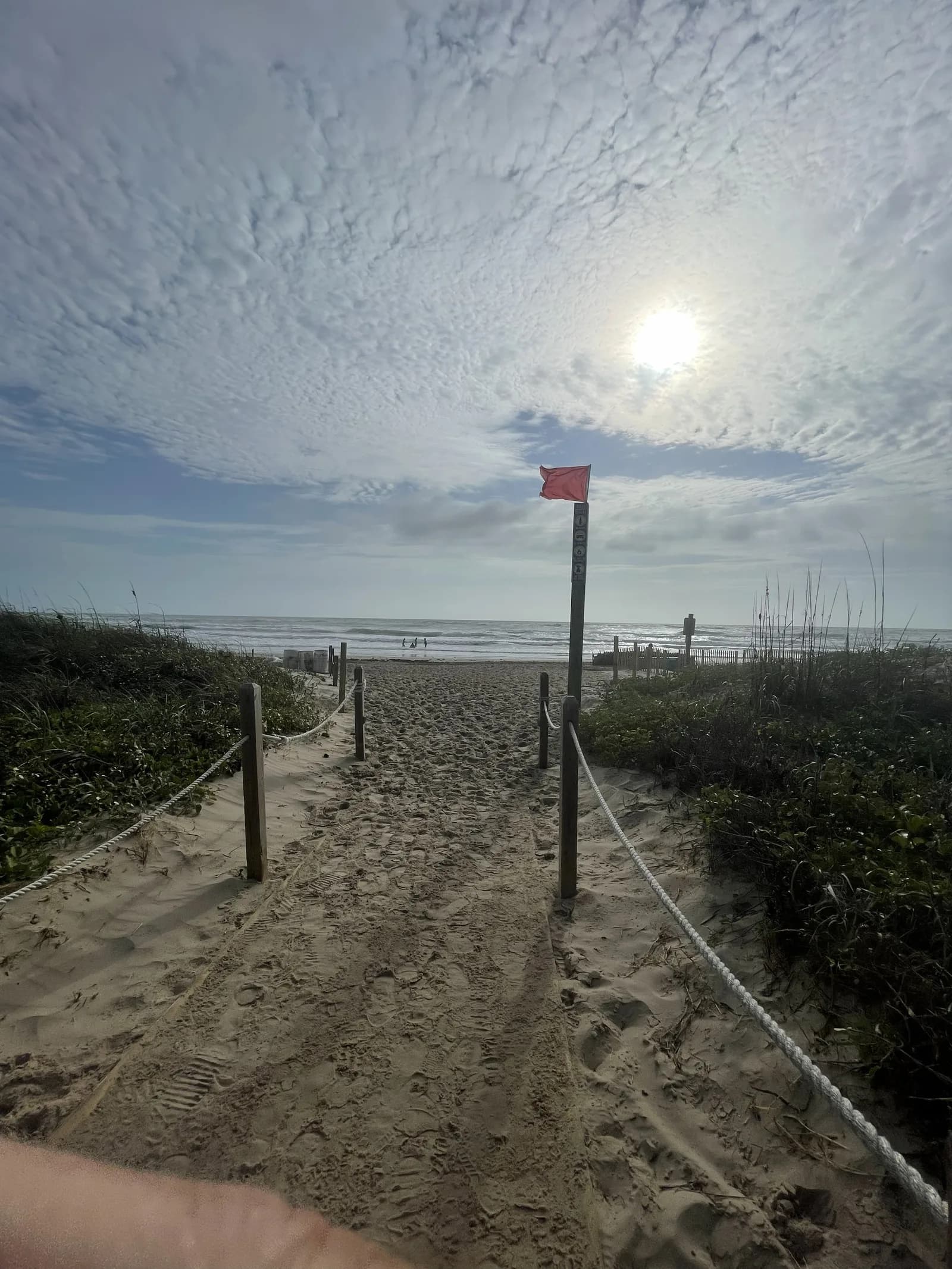 End of the boardwalk opening onto the sand with the Gulf and a red flag in view